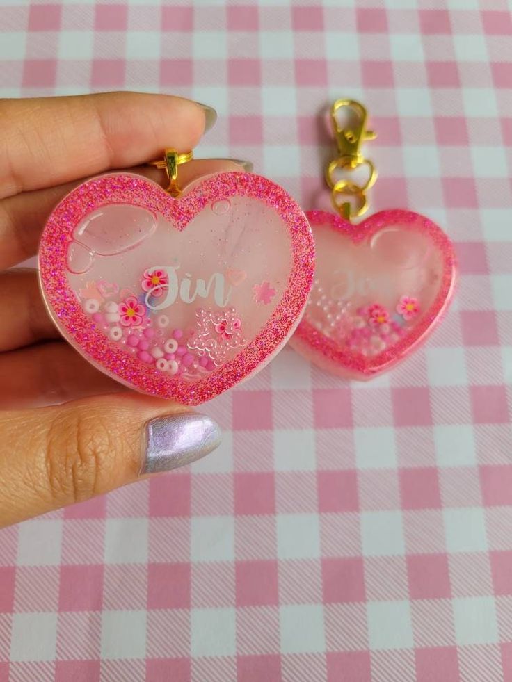 two pink heart shaped key chains on a checkered tablecloth with one being held in the other's hand