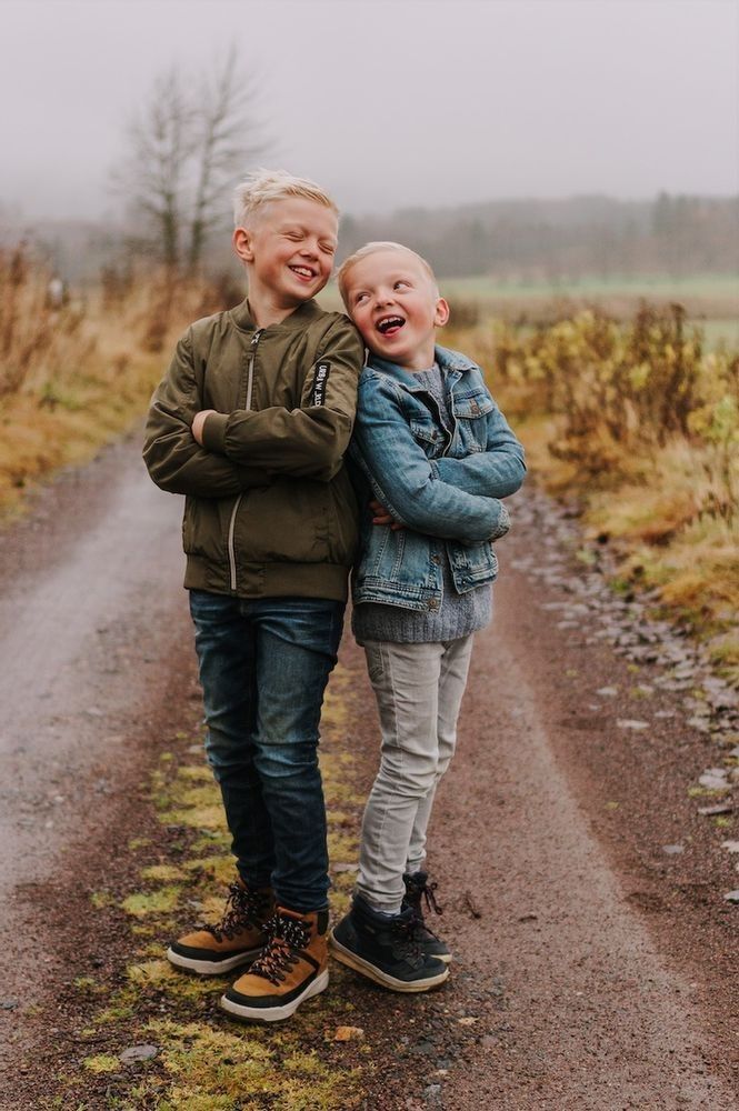 two young boys standing next to each other on a dirt road