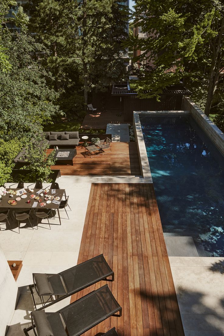 an aerial view of a swimming pool and patio area with lounge chairs, tables, and trees