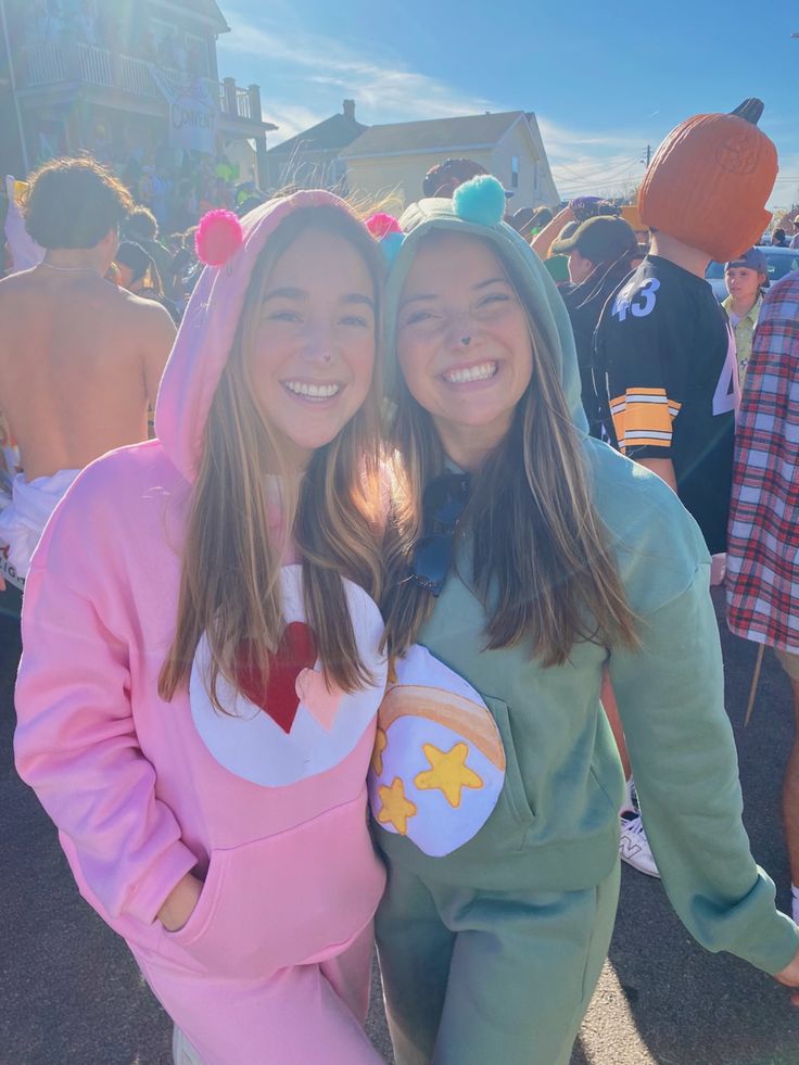 two girls in costumes posing for the camera at an outdoor event with other people behind them