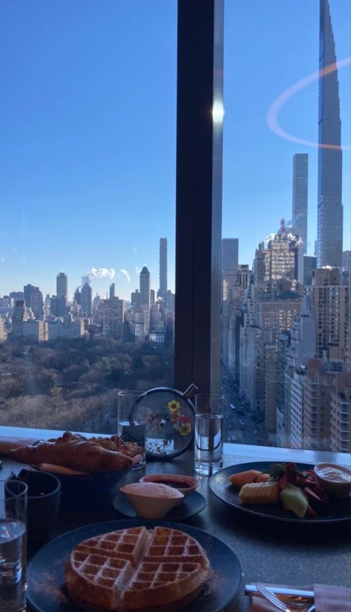 a table with plates of waffles and other food in front of a window overlooking the city