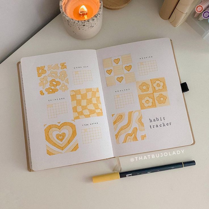 an open notebook sitting on top of a table next to a candle and some markers