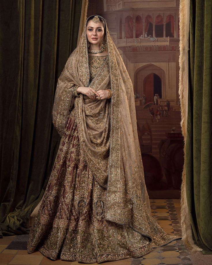 a woman standing in front of green curtains wearing a bridal gown and headpiece