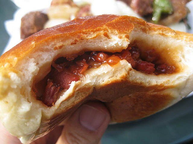 a hand holding a hot dog bun with meat and cheese in it's center