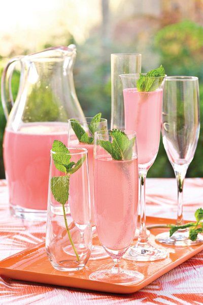 three glasses filled with pink liquid and mint sprigs sit on a wooden tray