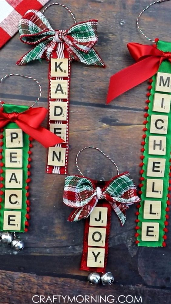 christmas ornaments made from scrabble tiles and ribbon hang on a wooden surface with the word peace, joy