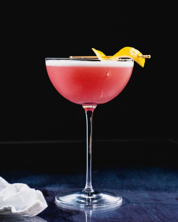 a pink cocktail with a yellow bird on the top and garnished in lemon