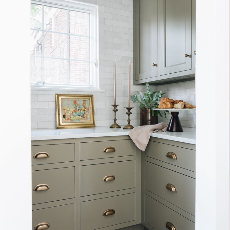 a kitchen with gray cabinets and gold pulls on the countertop, along with candles