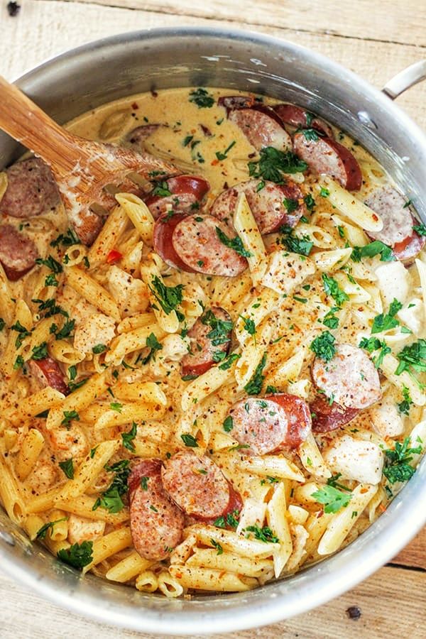 pasta with sausage, tomatoes and parsley in a pan on a wooden table top