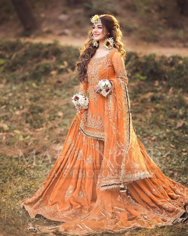 a woman in an orange dress standing on the grass with her hair down and flowers in her hair