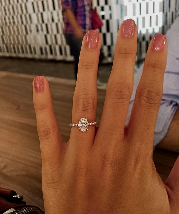 a woman's hand with a diamond ring on her left hand and a man in the background