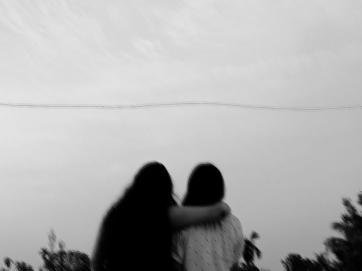 two people standing next to each other in front of a kite flying high up in the sky