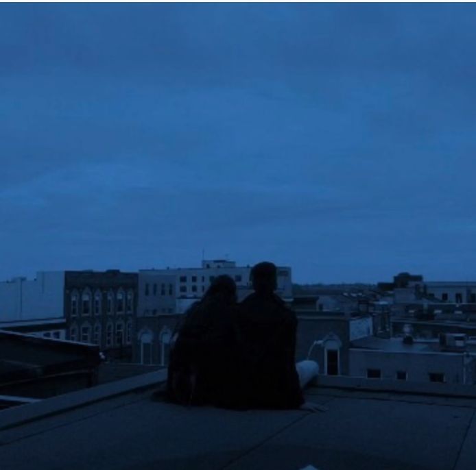 two people sitting on top of a roof at night