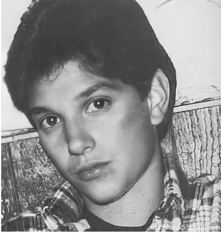 a black and white photo of a young man with short hair wearing a plaid shirt