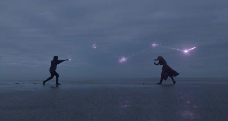 two people are walking on the beach at night with sparklers in the sky above them