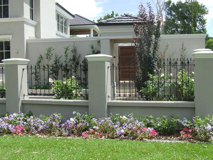 a white house with flowers in front of it and a black fence around the yard