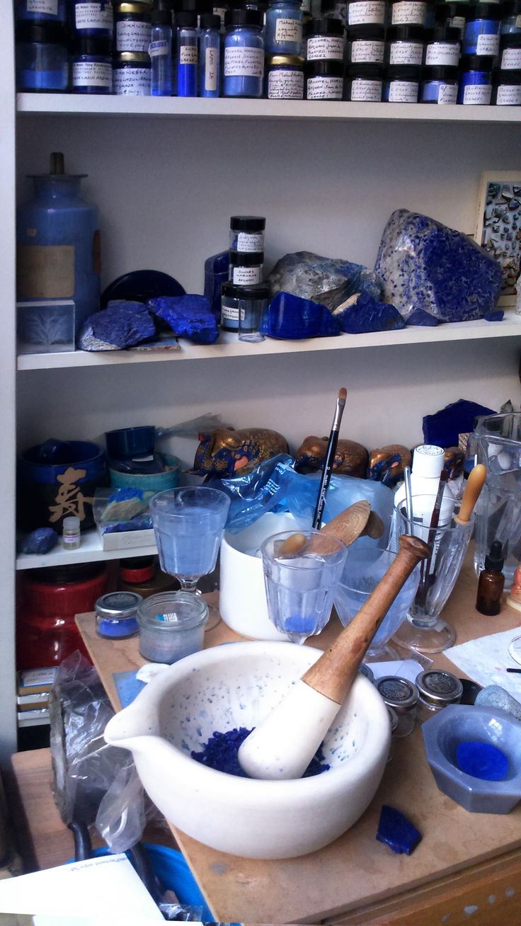 a wooden table topped with bowls filled with blue liquid and other items next to shelves