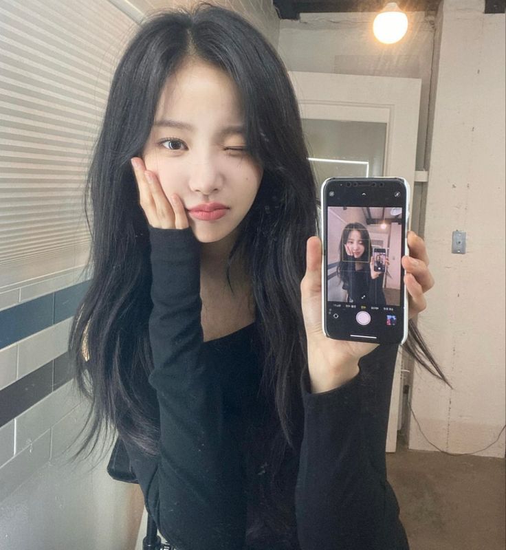 a woman taking a selfie with her cell phone in front of her face and wearing a black top