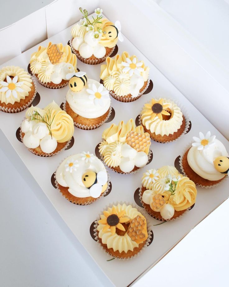 twelve cupcakes in a white box decorated with yellow and white frosting flowers