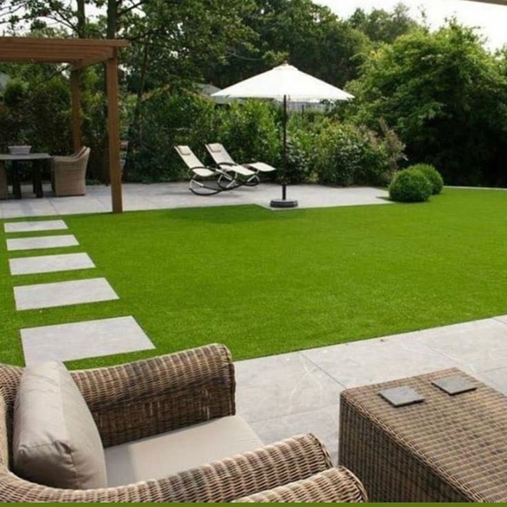 an outdoor patio with wicker furniture and umbrellas on the grass, surrounded by greenery