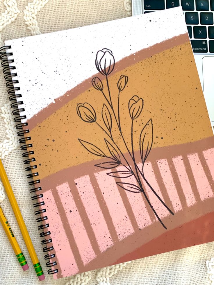 a notebook with flowers on it next to a laptop computer and pencils in front of it