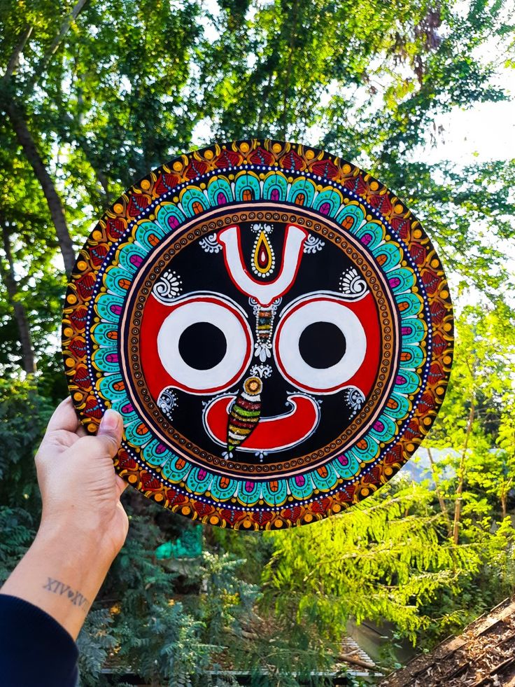 a person holding up a colorfully decorated plate in front of some trees and bushes