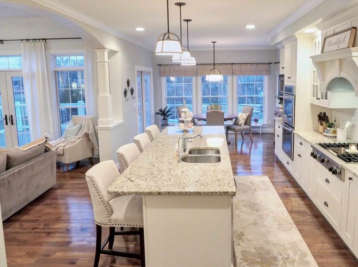 a large open concept kitchen and living room with white cabinets, marble counter tops and hardwood floors