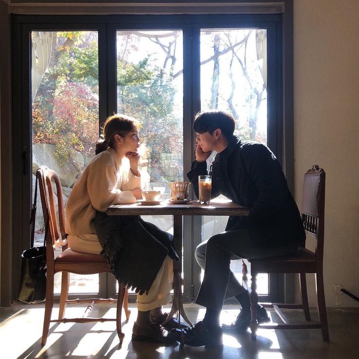 a man and woman sitting at a table in front of a window with the sun shining through