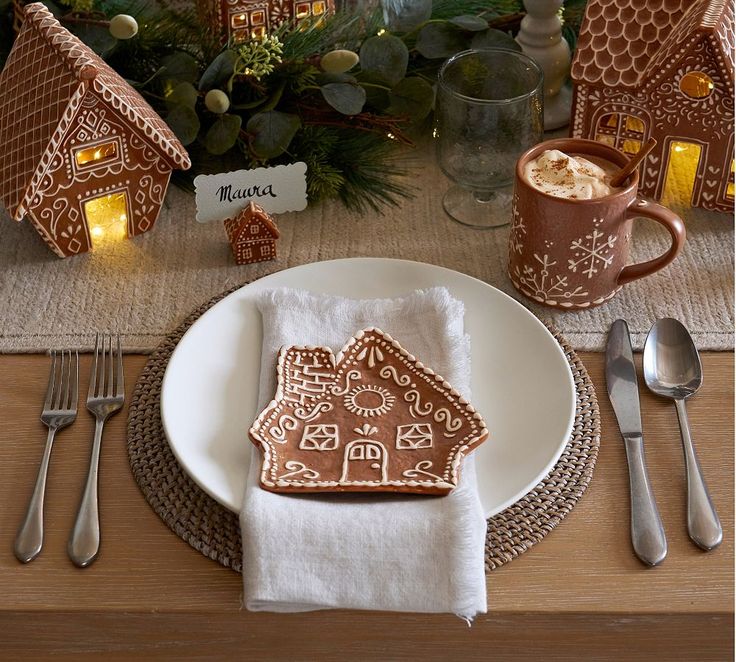 a plate with a gingerbread house on it and silverware next to the table