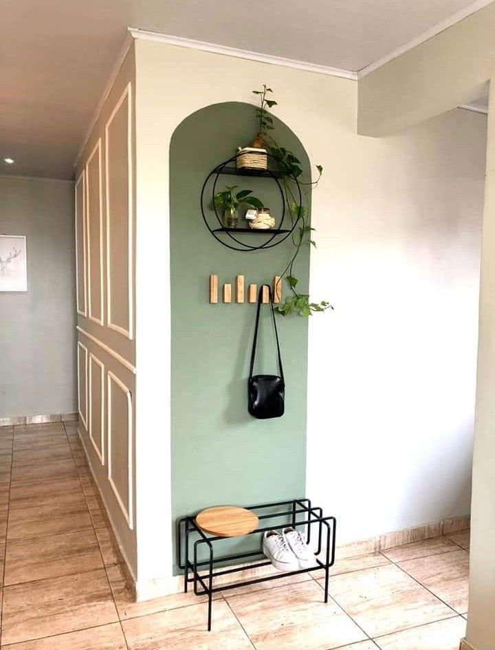 a green wall with some plants on it and a black shelf in the corner that holds two pots