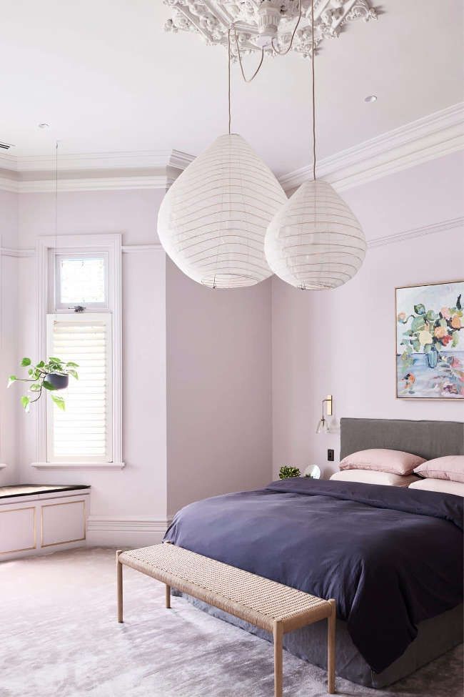 a bedroom with pink walls and two lamps hanging from the ceiling over the headboard