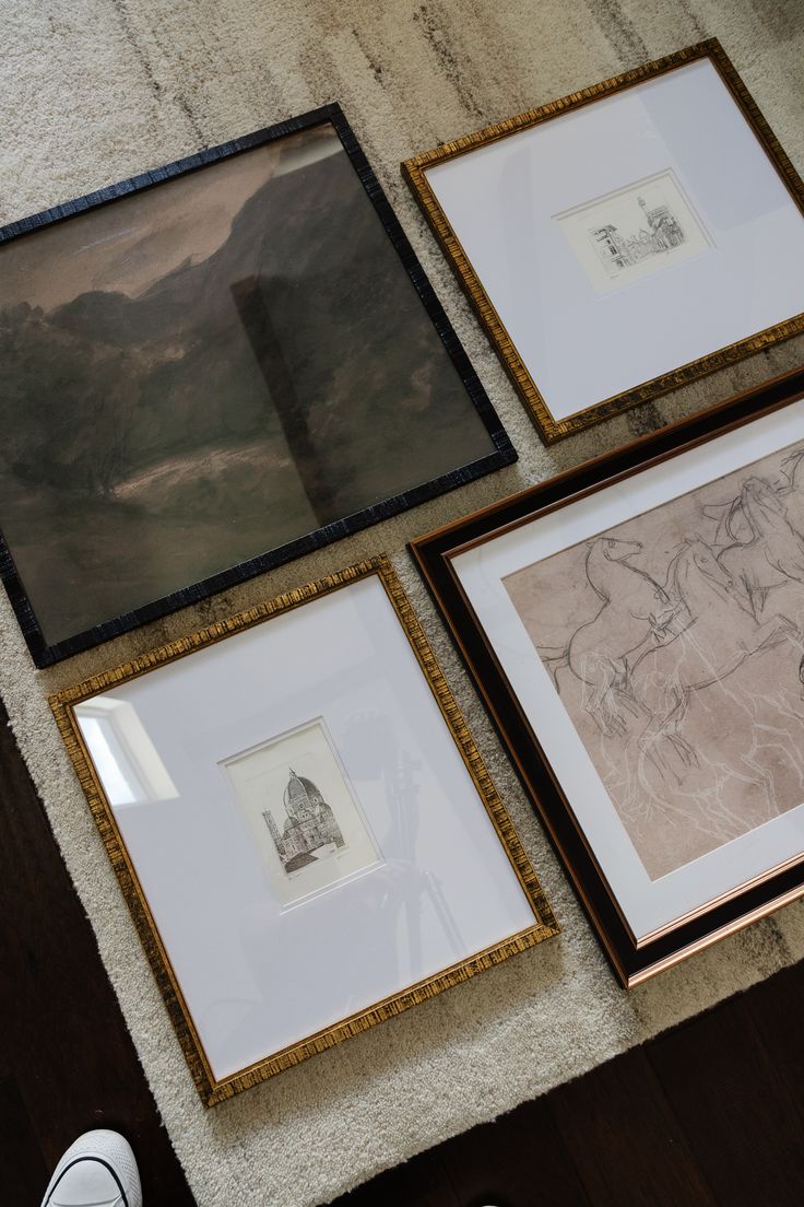 three framed pictures are on the floor next to a pair of shoes and a rug