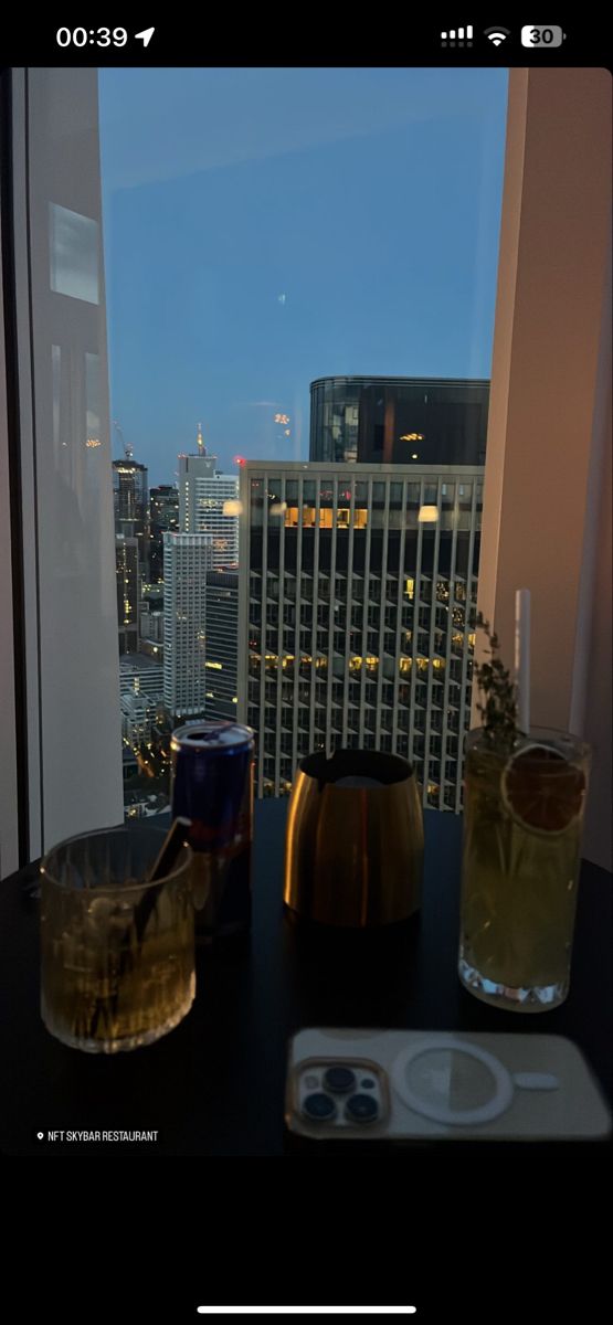 two drinks are sitting on a table in front of a window overlooking the city at night