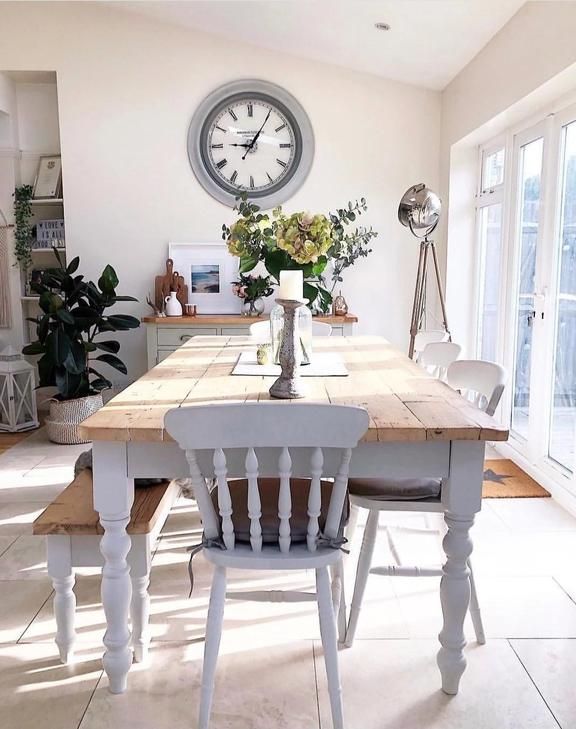 a dining room table with two chairs and a clock on the wall above it in front of windows