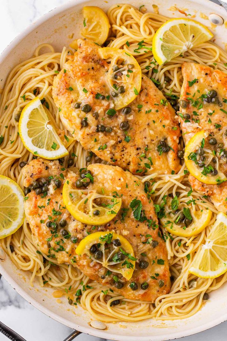 chicken with lemons and capers in a white skillet on a marble surface