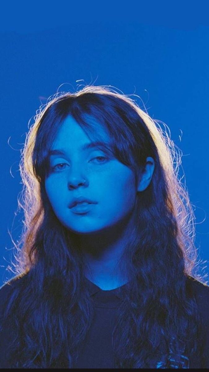 a woman with long hair standing in front of a blue background and looking at the camera