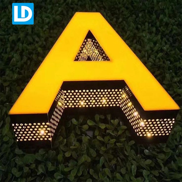 a yellow light up sign sitting on top of some green grass with bushes in the background