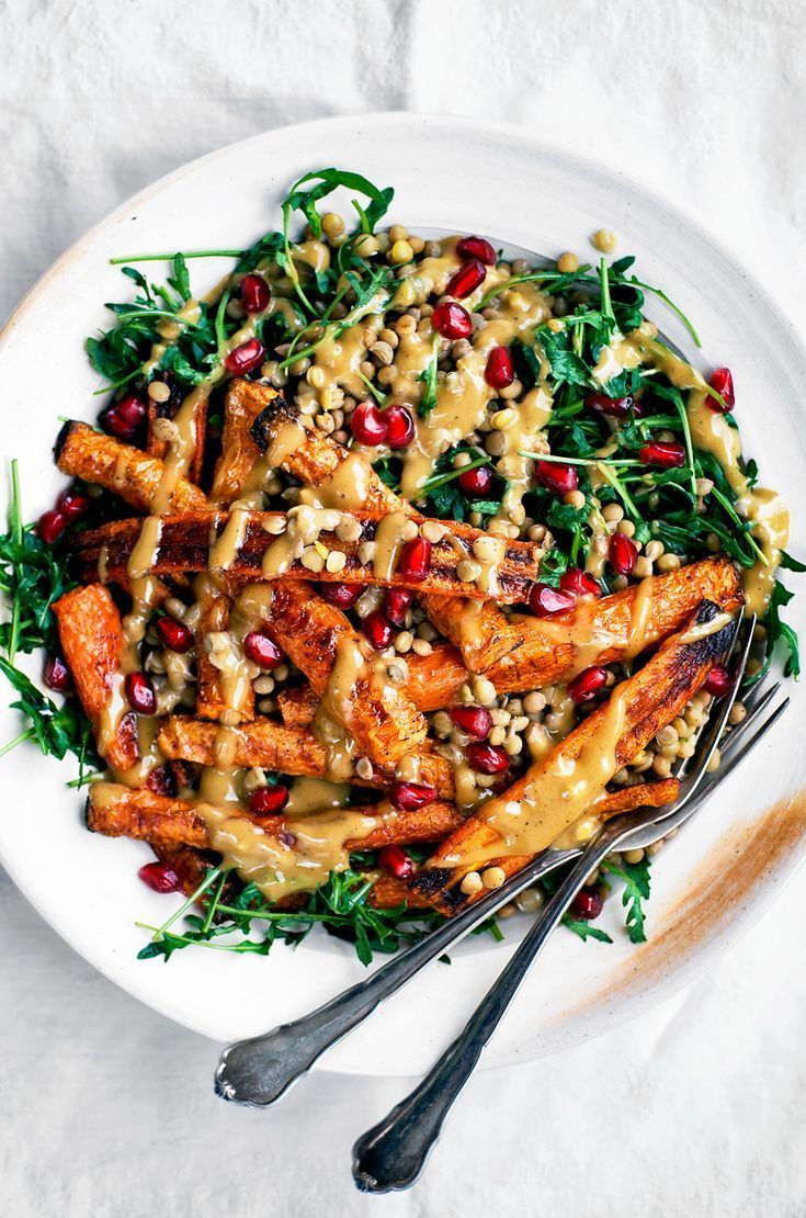 a white plate topped with carrots covered in dressing and garnished with pomegranate