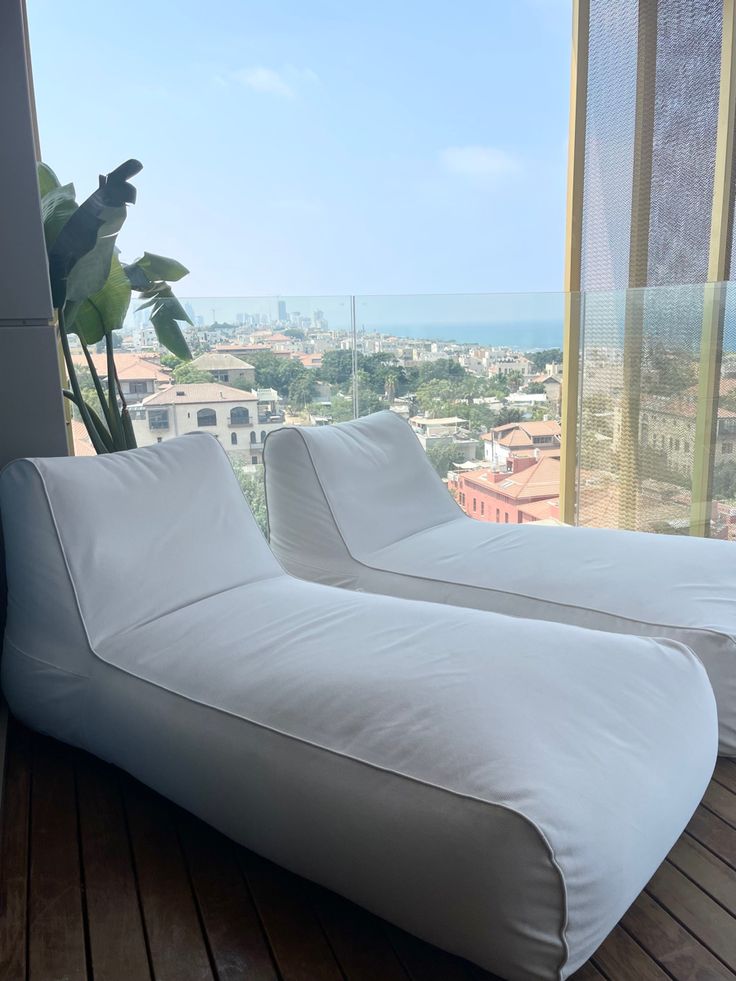 two white couches sitting on top of a wooden floor next to a large window