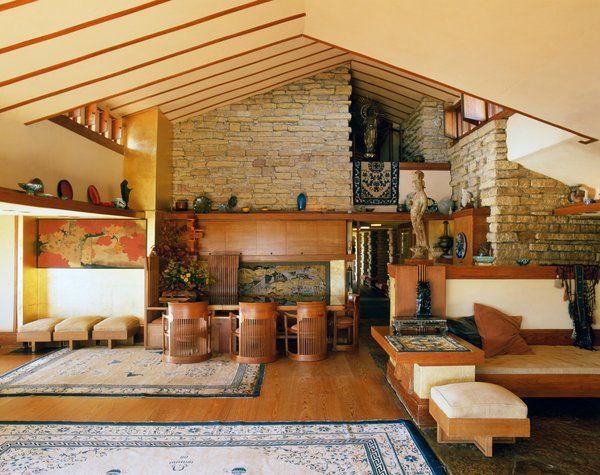 a large living room with wooden floors and stone fireplace in the center surrounded by wood paneling