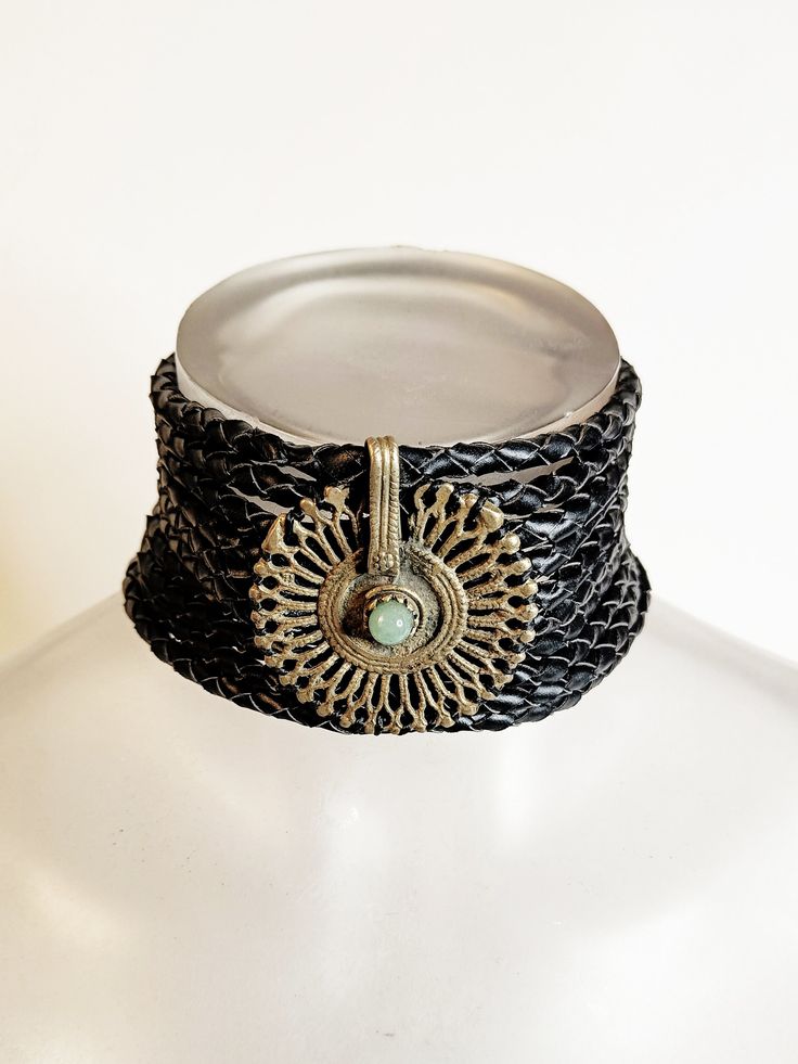 Discover the enchanting allure of our one-of-a-kind bohemian choker, meticulously handcrafted for the empowered woman with a penchant for unique style. This exquisite piece features a vegan braided leather band that gracefully adorns your neck, offering a comfortable and ethical fashion choice. At the heart of the choker lies an antique tribal central piece, boasting a stunning piece of jade with a rich history that adds depth and storytelling to your ensemble. Measuring at a versatile length, t Handmade Adjustable Choker For Festivals, Unique Brass Choker For Festivals, Bohemian Brass Choker Jewelry, Handmade Adjustable Vintage Choker, Adjustable Bohemian Choker Jewelry, Unique Adjustable Choker With Variations, Unique Adjustable Choker With Unique Variations, Black Bohemian Bracelet Jewelry, Bohemian Choker With Unique Variations