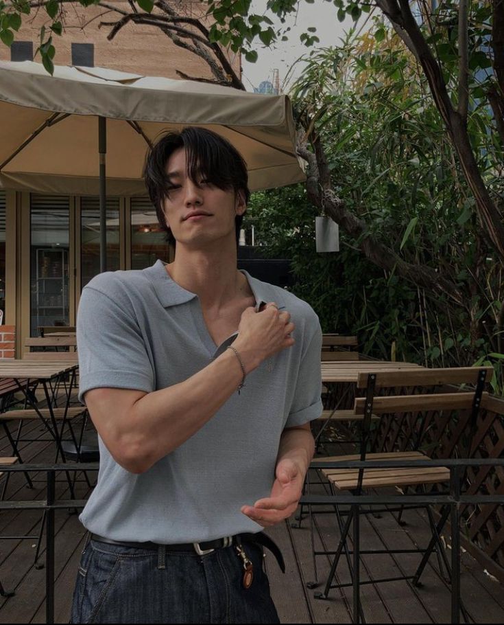 a young man is standing in front of an outdoor cafe with his arms crossed and looking at the camera