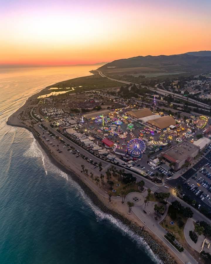 an aerial view of the beach and amusement park at sunset, with water in the foreground