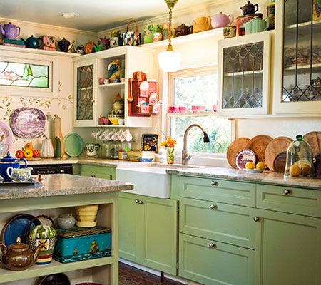 a kitchen with green cabinets and lots of dishes on the counter top in front of a window