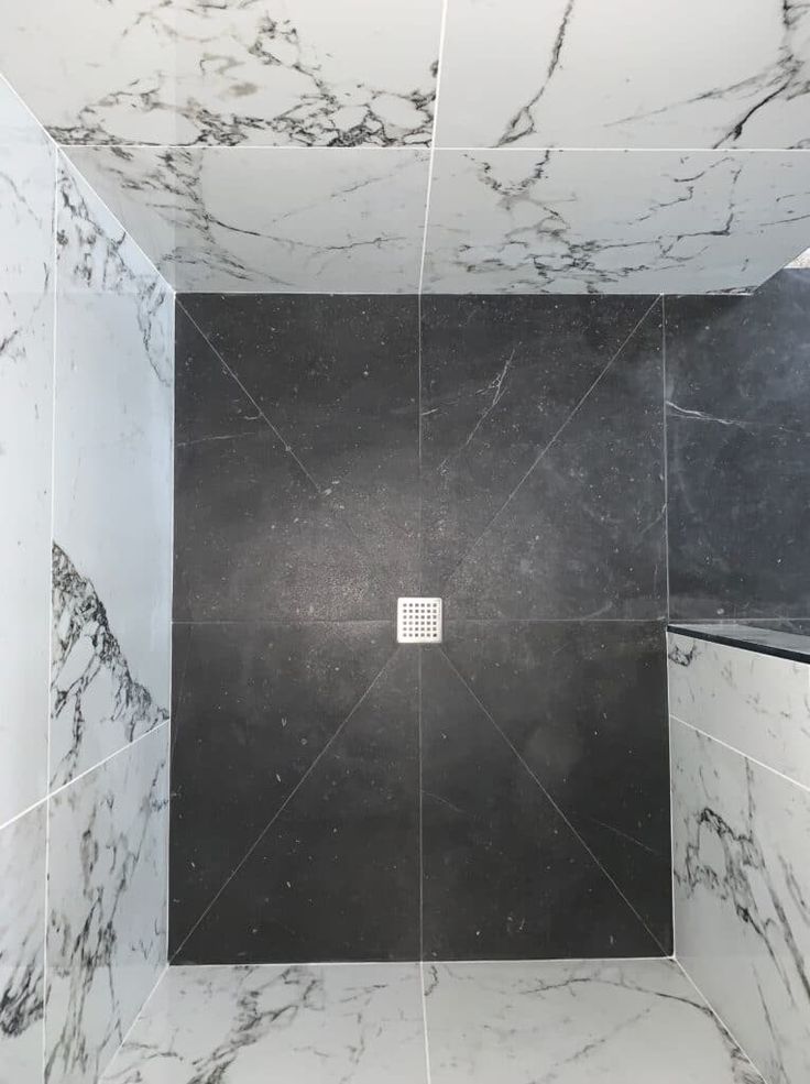 a black and white tiled shower stall with square drain in the center, surrounded by marble tiles