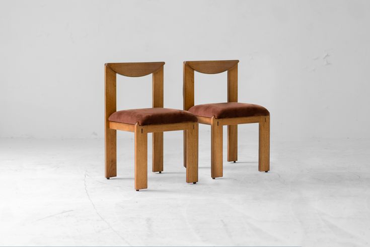 two wooden chairs sitting side by side on a white floor with one chair facing the other