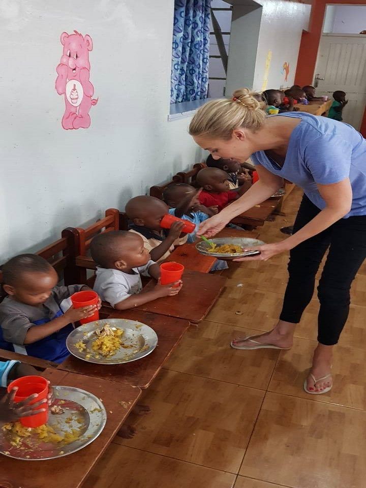 a woman is serving food to children at a long table in a room with wooden floors