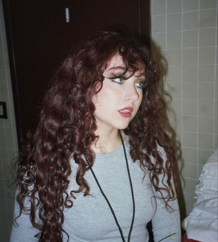 a woman with long red curly hair is looking at her cell phone in the bathroom