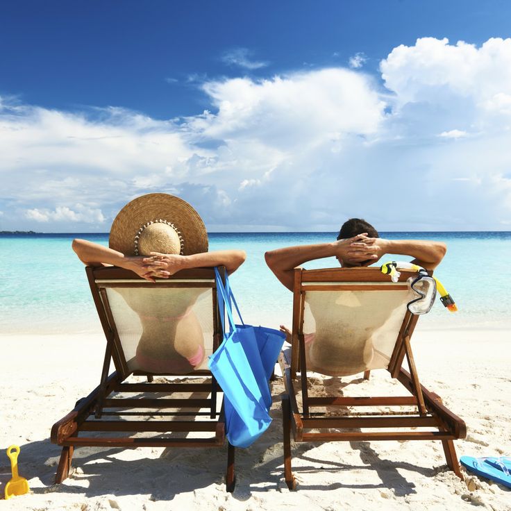 two people sitting in chairs on the beach with their backs to each other, facing the ocean