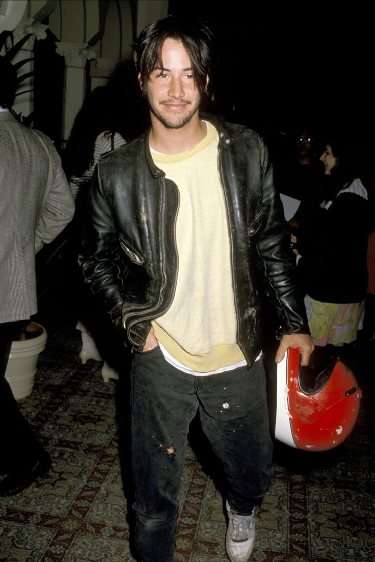 a man in black leather jacket standing next to a red and white motorcycle helmet on the floor